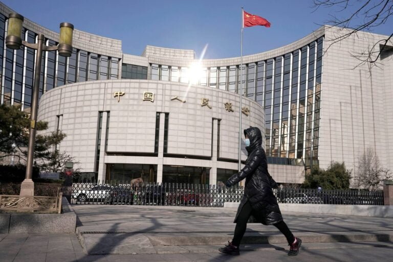 FILE PHOTO: Man wearing a mask walks past the headquarters of the People's Bank of China, the central bank, in Beijing